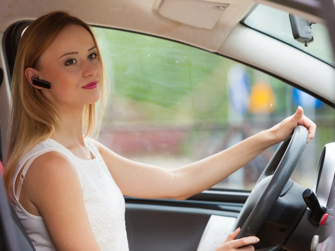 O femeie care conduce o mașină si poarta o casca bluetooth handsfree si o casca bluetooth profesionala