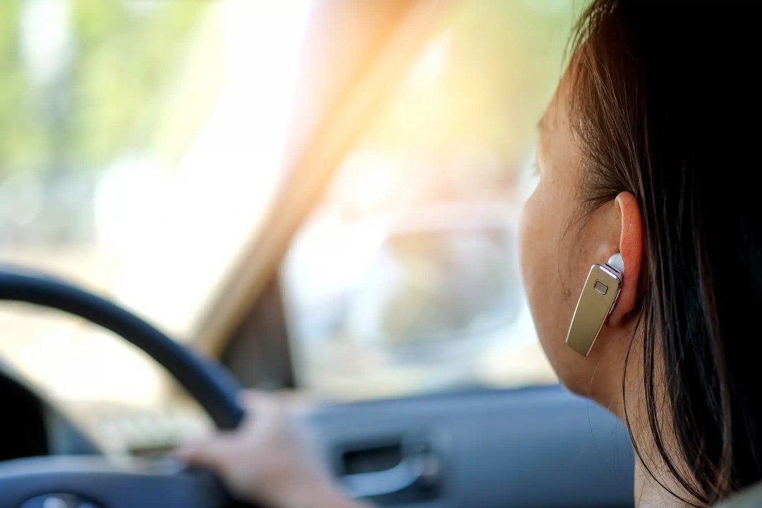 O femeie care conduce o mașină si poarta o casca bluetooth handsfree si o casca bluetooth profesionala