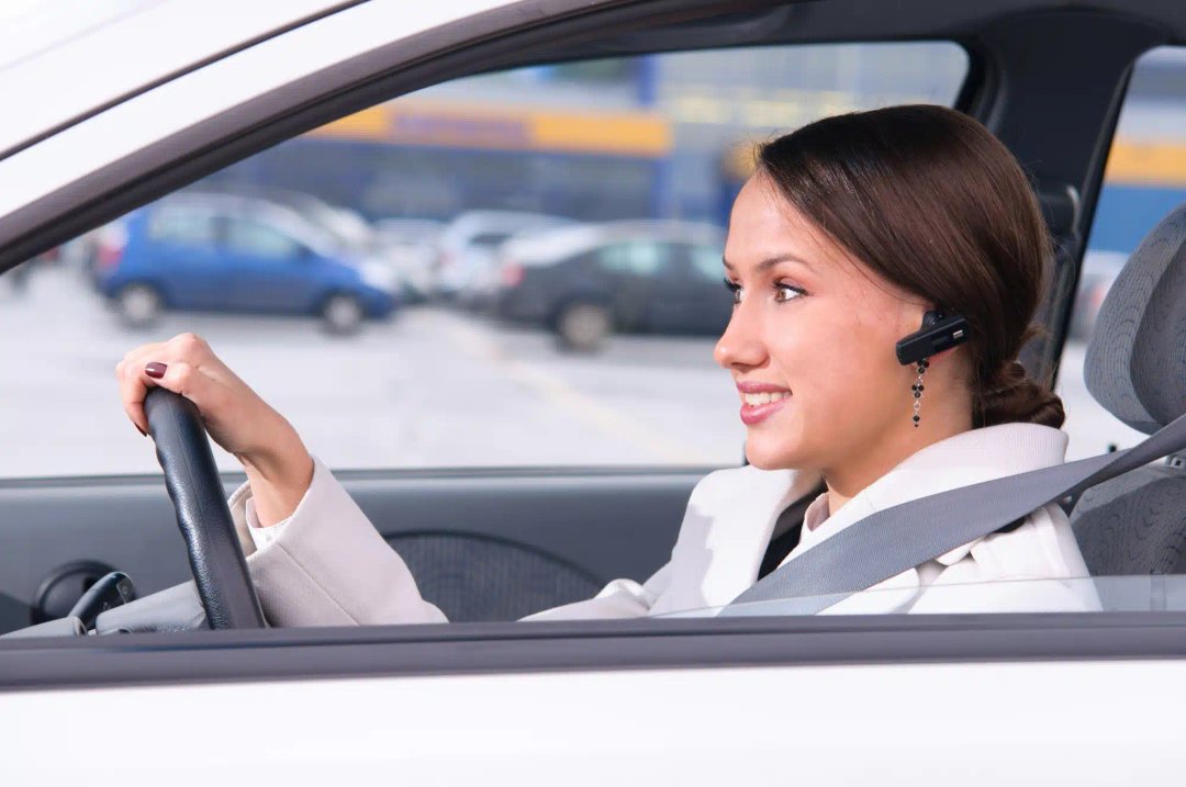 O femeie care conduce o mașină si poarta o casca bluetooth handsfree si o casca bluetooth profesionala