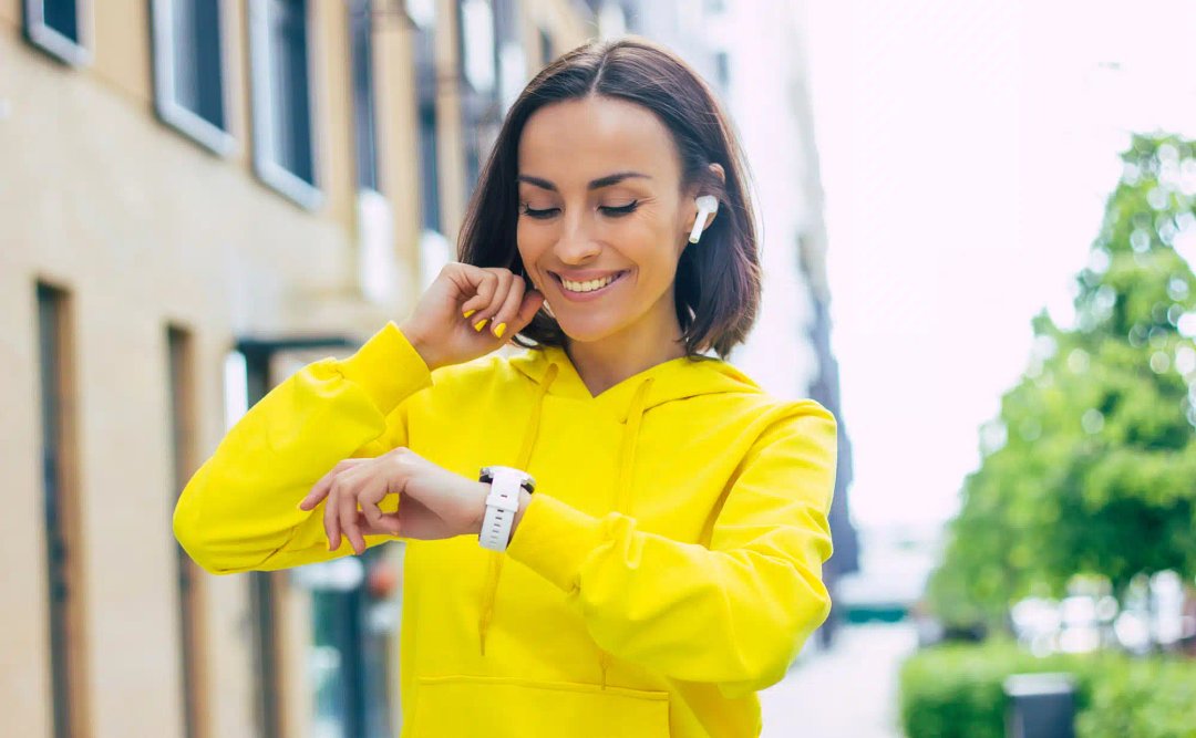 O tânără care poartă un hanorac galben verificându-și ceas smartwatch dama