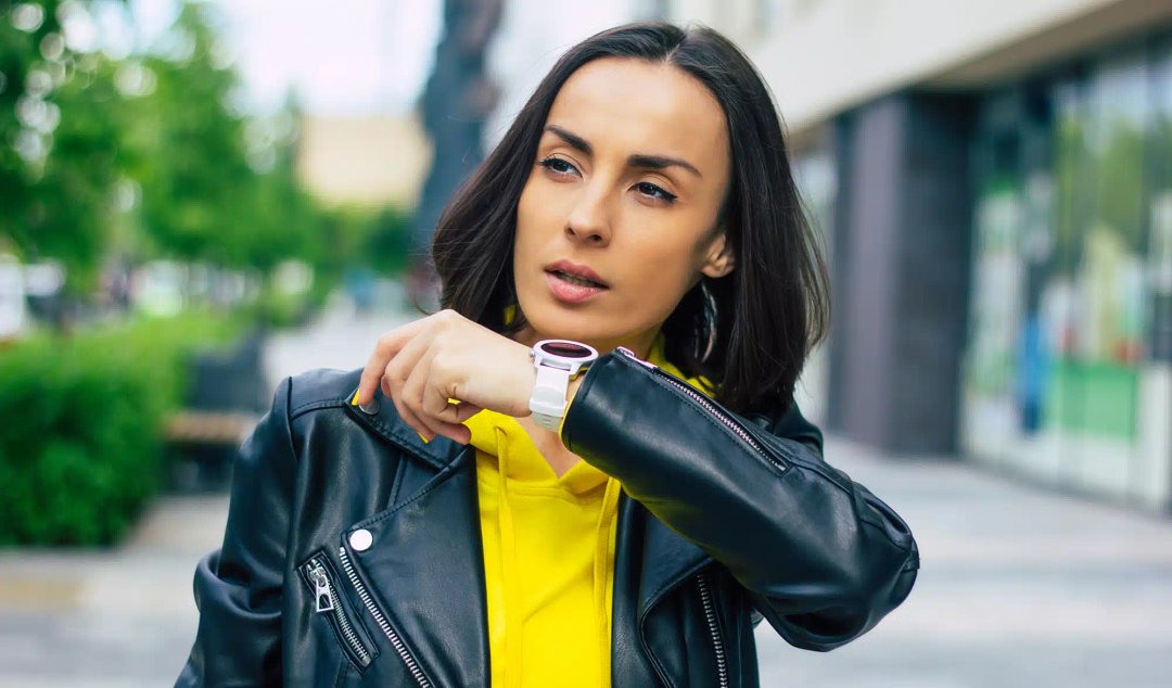 O femeie care poartă o geacă de piele și o cămașă galbenă se uită la ceas smartwatch dama elegant.
