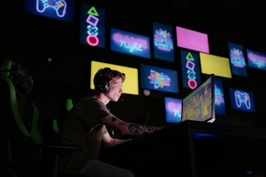Tânăr concentrat în joc, purtând căști gaming Bluetooth cu latență scăzută și lumini ambientale