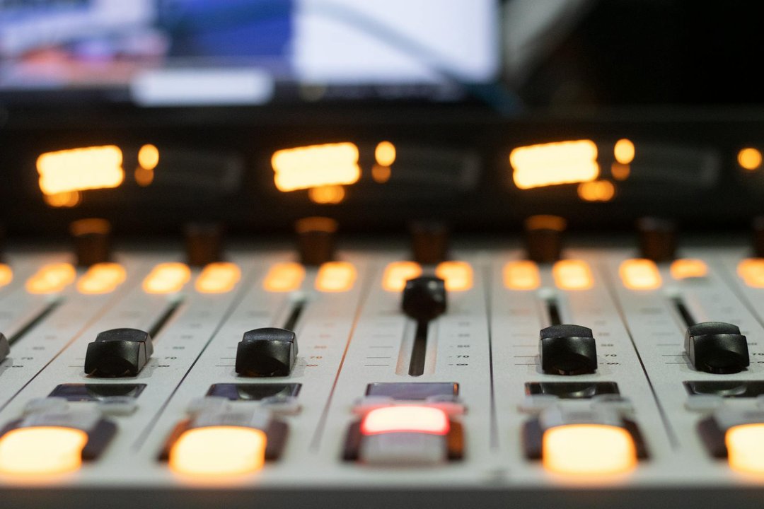 Detaliu cu o pereche de căști de studio profesionale așezate pe o consolă de mixaj audio iluminată.